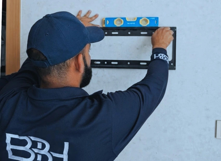 Professional technician providing handyman services in Dubai, mounting a TV on a villa wall.