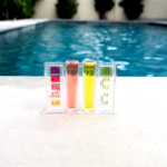 A professional swimming pool water testing kit showing chlorine and pH levels next to a clear blue villa pool in Dubai.