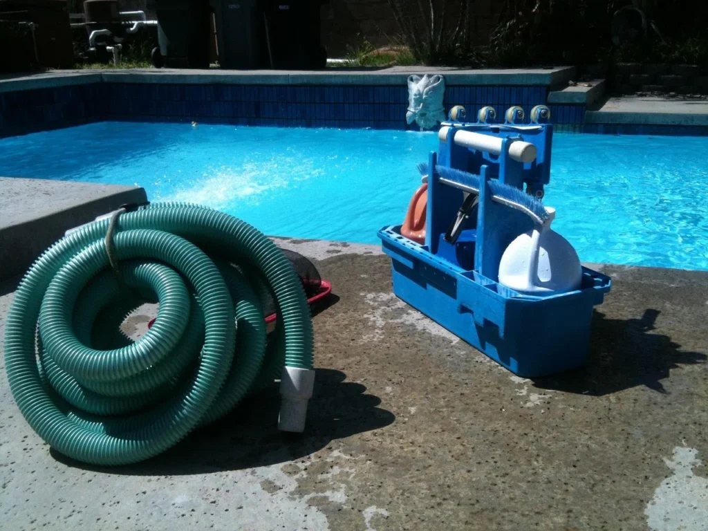 Professional pool cleaning equipment and vacuum hose poolside, indicating a need for structural pool renovation or deep maintenance.