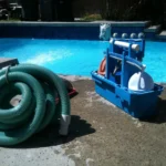 Professional pool cleaning equipment and vacuum hose poolside, indicating a need for structural pool renovation or deep maintenance.